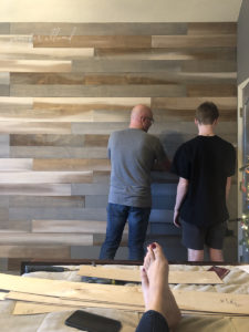 father and son creating a wood wall in teenage sons bedroom while wife watches