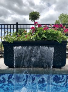 black painted planters with waterfall coming out of it and flowers planted in the top