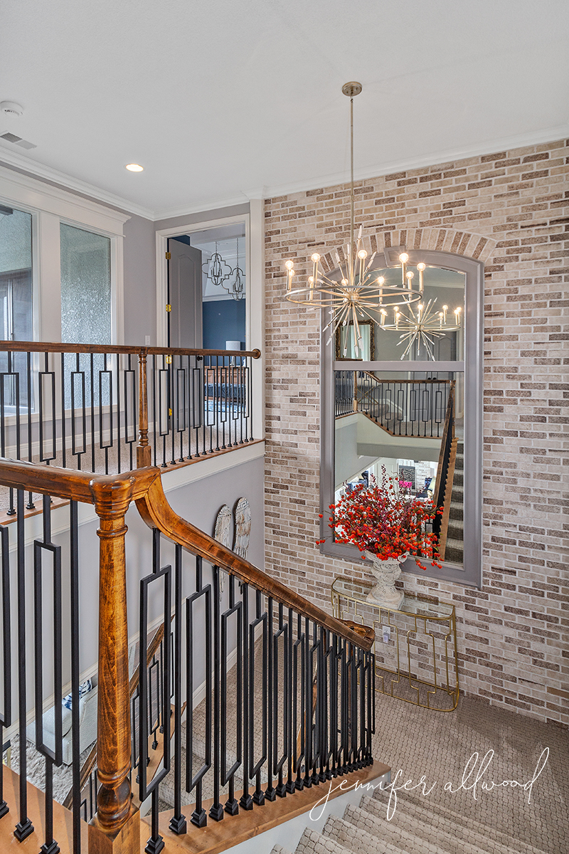 light brick wall, gold chandelier, modern spindles, and light stair carpet